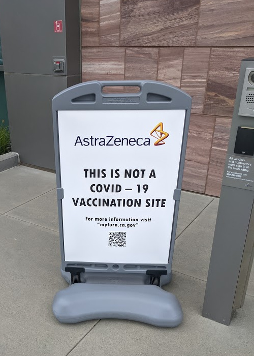 signboard by a security gate. Sign reads: AstraZeneca. This is Not a COVID-19 vaccination site