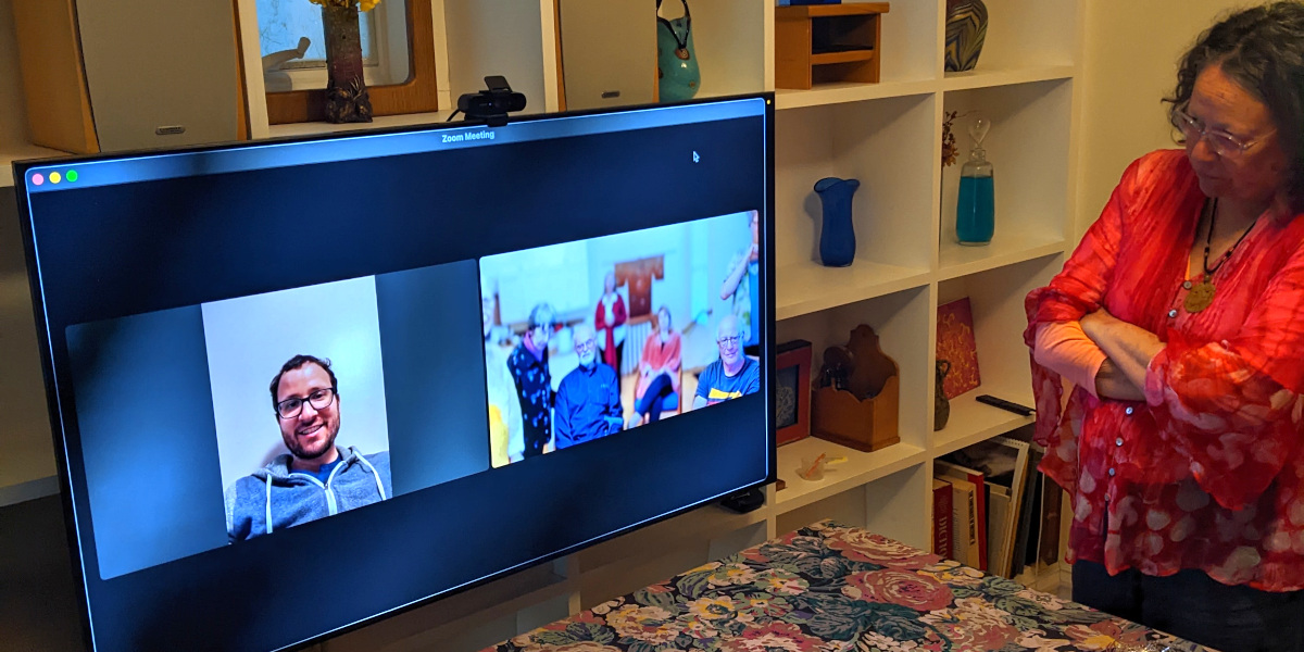 [photo: a computer monitor showing a Zoom meeting; next to the monitor, an aunt]