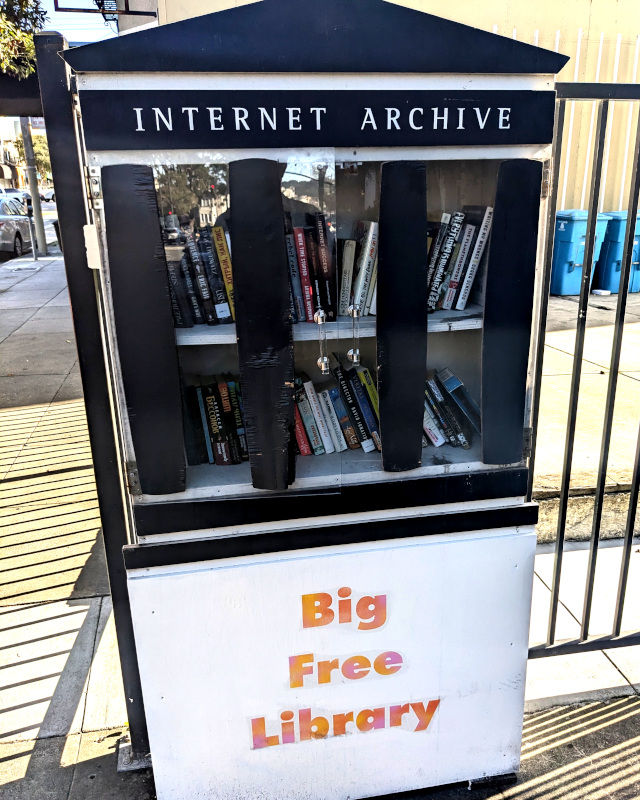 a big cabinet of books outside on a side street. it's labeled Internet Archive Big Free Library. inside are many books including a surprising number with Cyrillic; also a copy of Poundstone's How Would You Move Mt Fuji