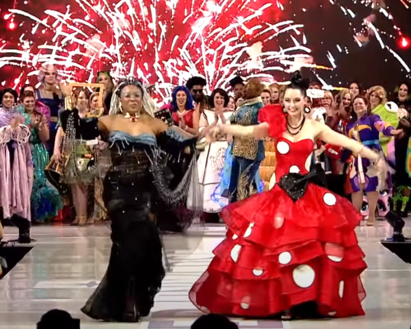 a fashion runway with many people in snazzy outfits. in the foreground are two winners, one whose outfit evokes Storm from the X-Men, the other's Minnie Mouse