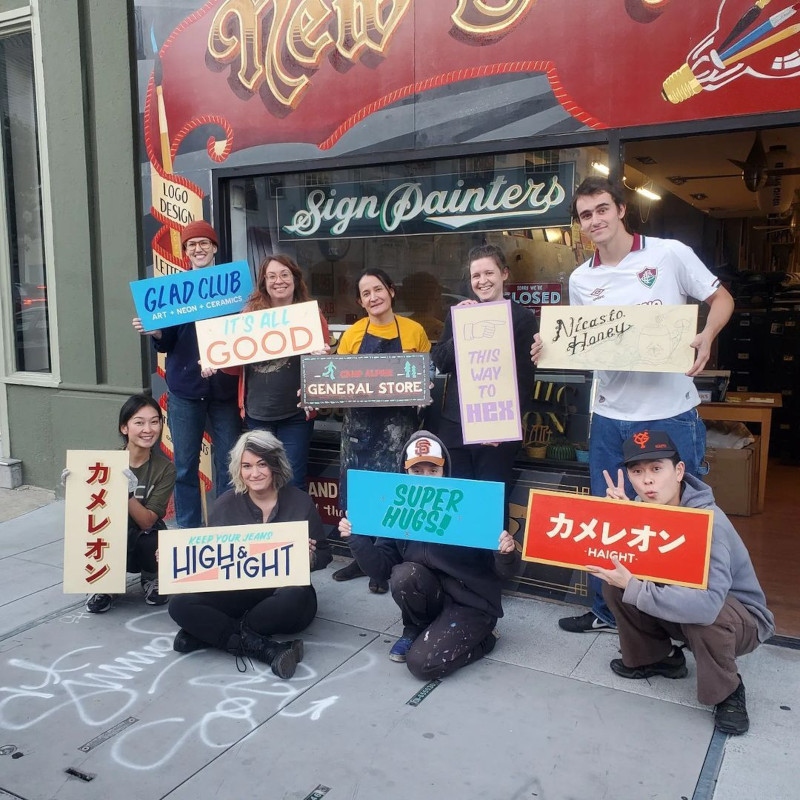smiling artists holding up hand-painted lettered signs