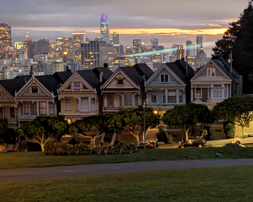 nighttime (well, dawn-ish) photo of San Francisco's “Painted Ladies” houses but with light beams visible behind them