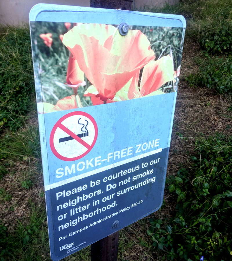 photo of old sign that reads "Smoke-Free Zone / Please be courteous to our neighbors. Do not smoke or litter in our surrounding neighborhood. Per Campus Administrative Policy 550-10 UCSF University of California San Francisco"