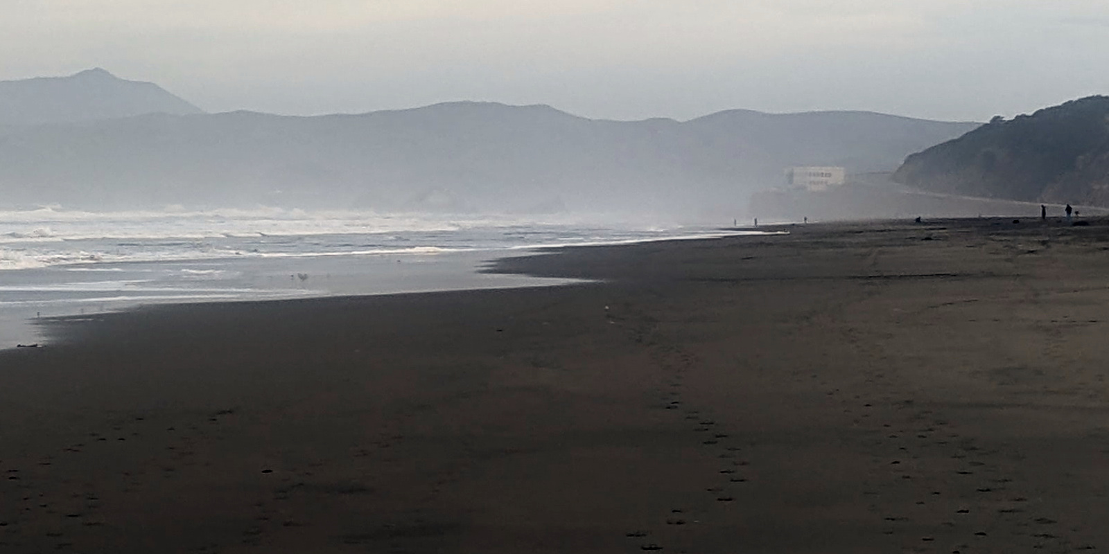 photo: wintry beach scene: sand, water, distant hills, gray sky