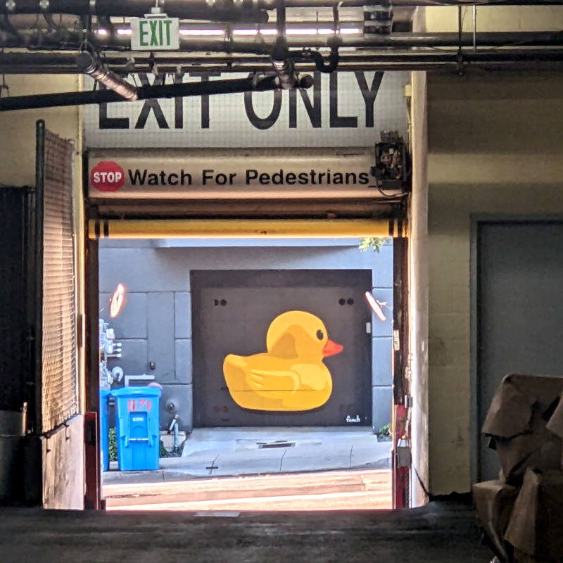 a parking garage exit door. out the exit door, there's recycling bins and a stencilly-looking rubber duck mural