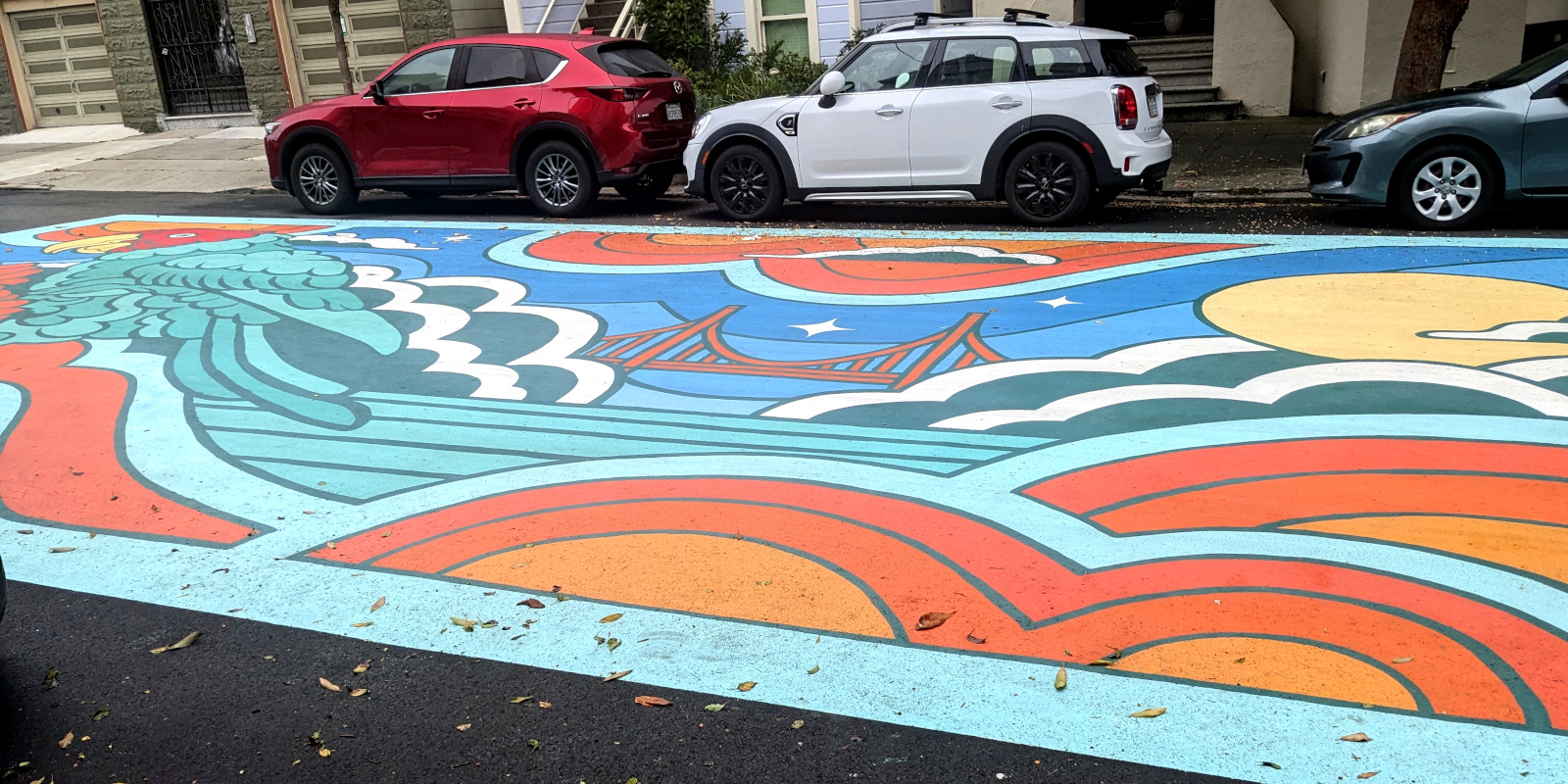 part of a big ground mural covering most of the width of a street; it shows the Golden Gate Bridge and a parrot