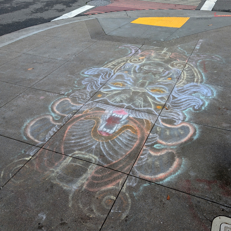 sidewalk chalk art sorta like the face of someone wearing elaborate headgear, until you realize it's meant to be viewed either this way or upside-down whence you'd see another face with other elaborate headgear; the 'elaborate headgear' is another face