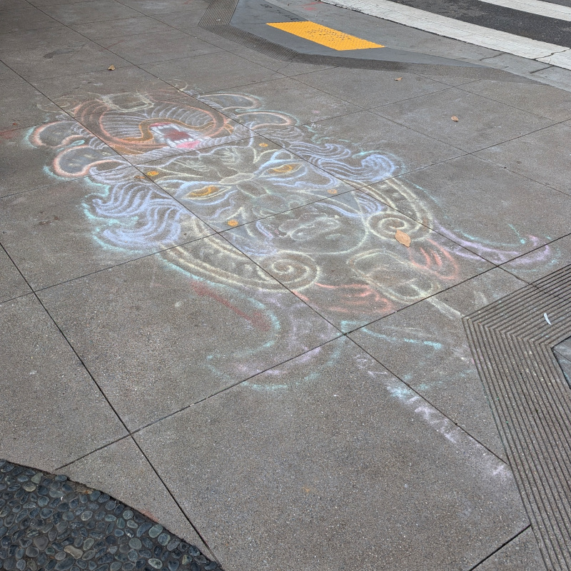 sidewalk chalk art sorta like the face of someone wearing elaborate headgear, until you realize it's meant to be viewed either this way or upside-down whence you'd see another face with other elaborate headgear; the 'elaborate headgear' is another face