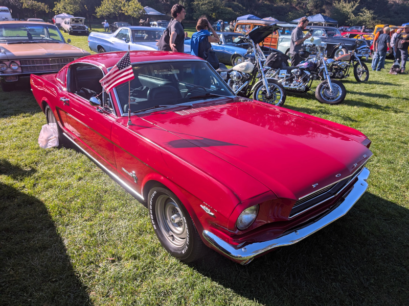 foreground: shiny red Mustang flying a USA flag from the antenna
