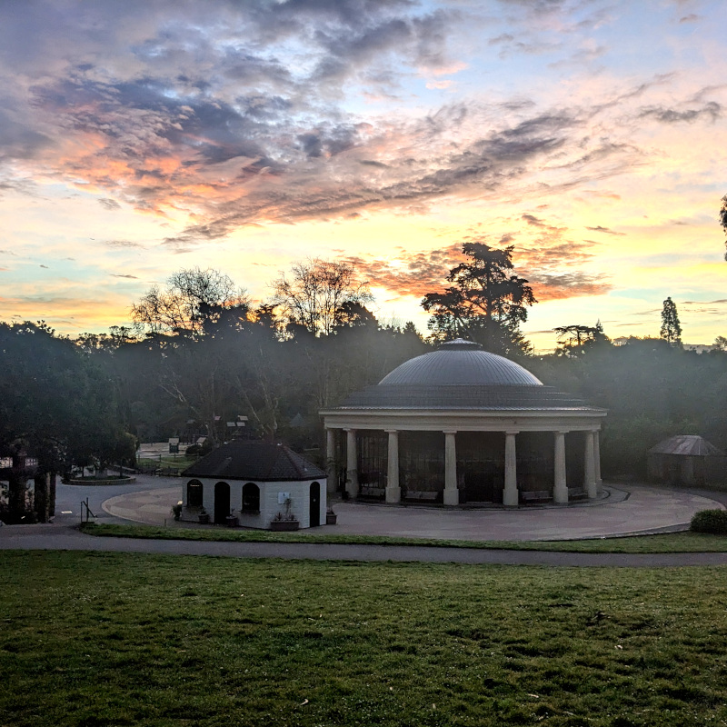 foreground: Carousel building at Koret playground. Background: silhouettes of trees against sunrise-colored clouds