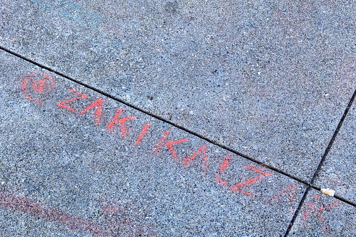 patch of sidewalk with hints of color, where chalk has mostly washed away. Most legible is a partial signature @zakikal...something