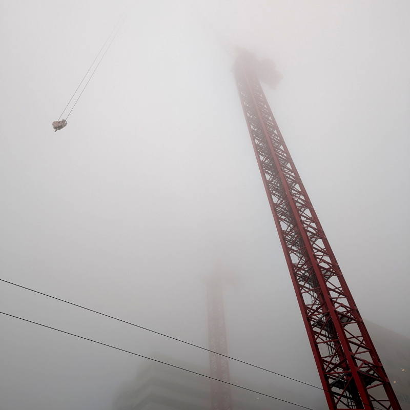 two crane towers fade up into fog. A crane hook descends from the fog. You can hazily make out a crane counterweight at the top of the nearer tower.