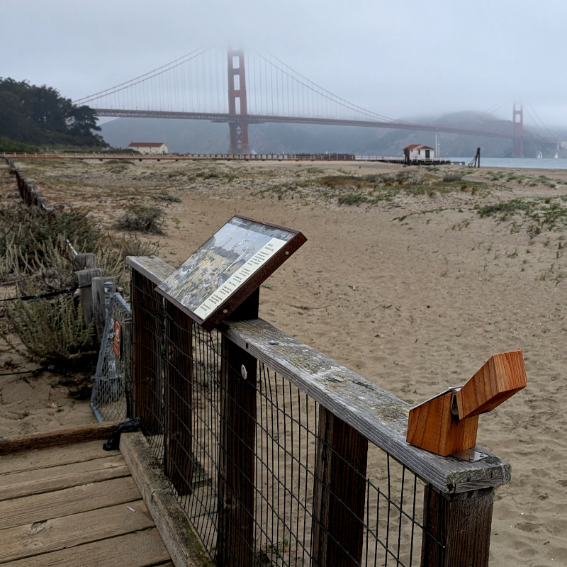 little wooden box atop a fence. also a beach and some bridge