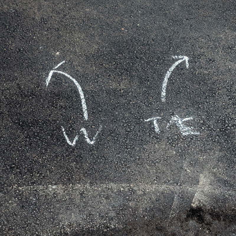 chalk marks on pavement. One set" "↖ W". The other: "↗ TE"