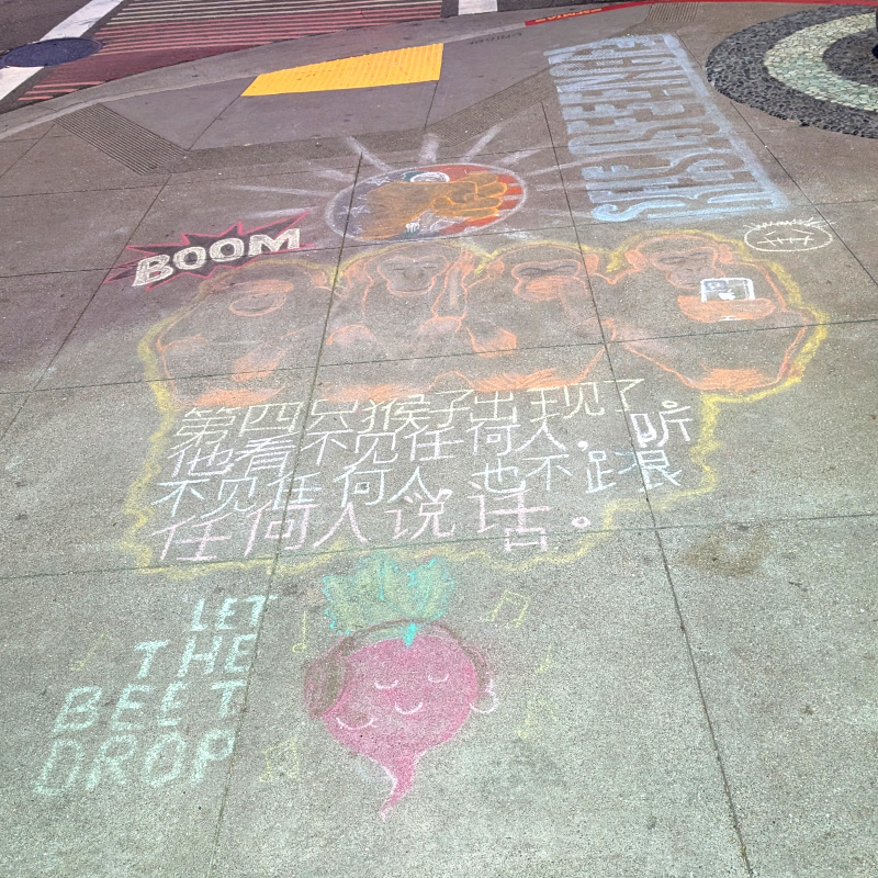 sidewalk chalk art. There's a cute anthropomorphic beat wearing headphones with text 'let the beet drop'. There are four monkeys: see no evil, hear no evil, speak no evil, and wearing headphones and staring at mobile phone oblivious to real world (no evil). There's Chinese text I can't translate, alas. And more.
