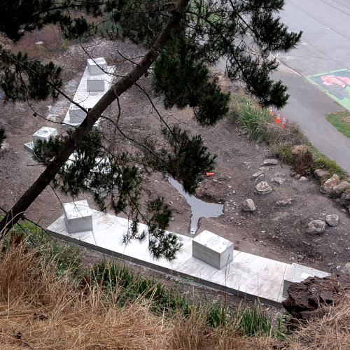 cement supports in a drained pond, seen from above with an annoying tree in the way. Individual parts of the supports are rectilinear solids; but they're arranged at angles to each other