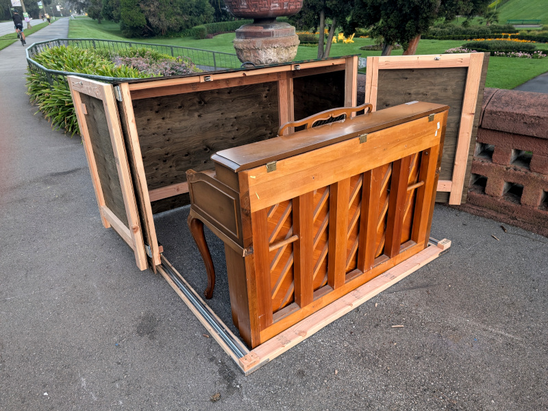 sidewalk piano partially enclosed by a big wooden box on rollers on tracks