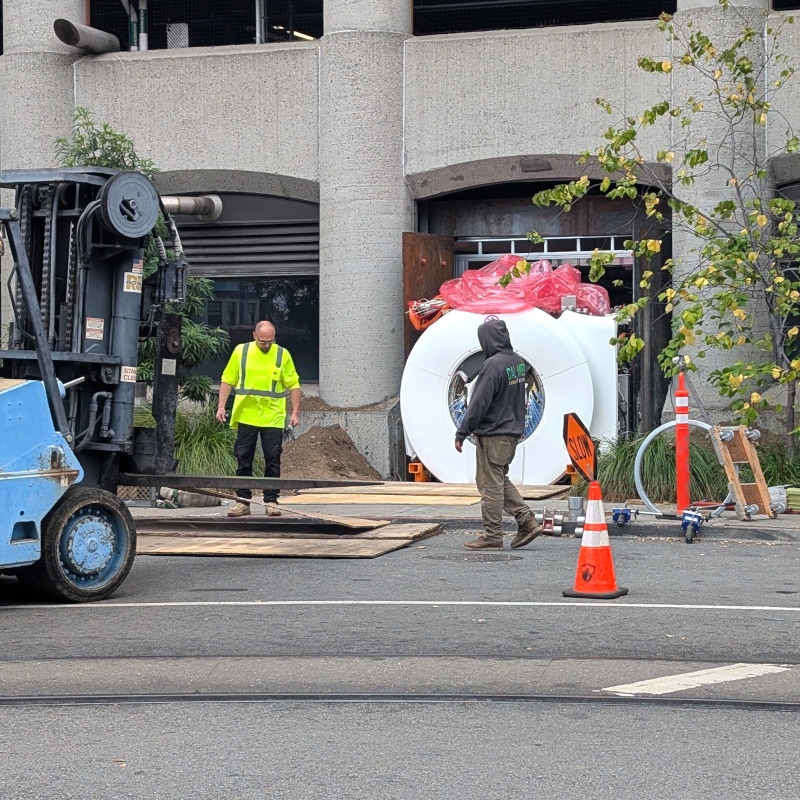 a big ol' medical scanner barely fitting through the whole in a wall. off to the side, a forklift stands ready. (could a little forklift handle a big ol' medical scanner? idk. anyhow