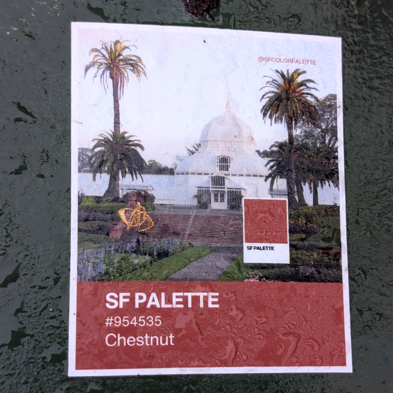 dew-speckled sticker on metal. the rectangular sticker's contents are a square image above some text. the square image is of the area in front of the SF Conservatory of Flowers. Overlaid on the steps is a polaroid-photo-looking white rectangle containing a brown square. The brown matches the color of the steps leading up to the Conservatory. The polaroid-photo-looking bottom has text: SF Palette. The top-right corner of the Conservatory photo has text: @sfcolorpalette. The text are at the bottom of the sticker has a brown background. Its text reads SF Palette / #954535 / Chestnut