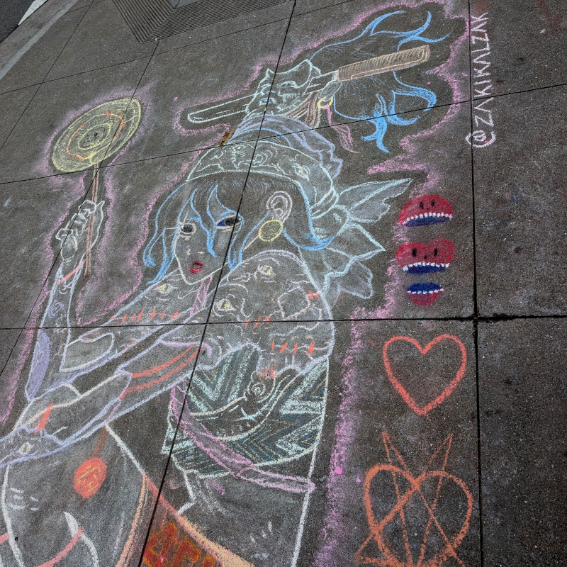 sidewalk chalk art. zooming in on top of skater. her hat appears to consist of a scarf, a cat(?) head, and a short sword through that cat head