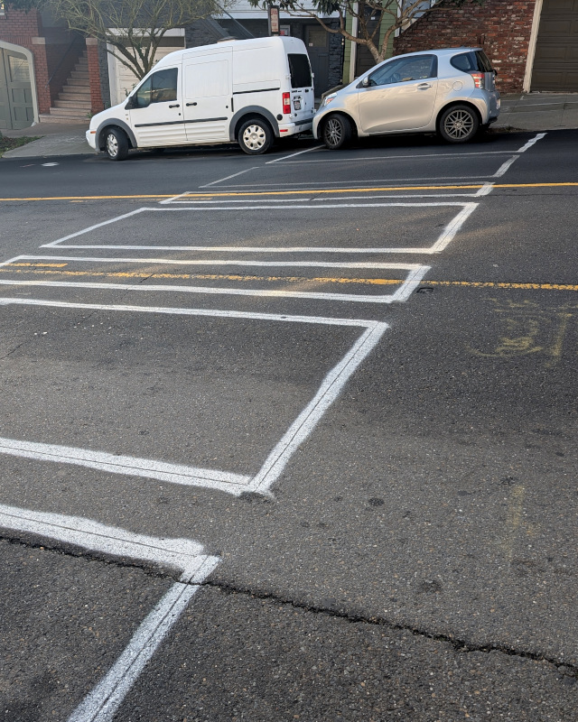 residential street on a hill. There are some rectangles painted on the street, suggesting that something about as wide as the street and about the length of a car is going in