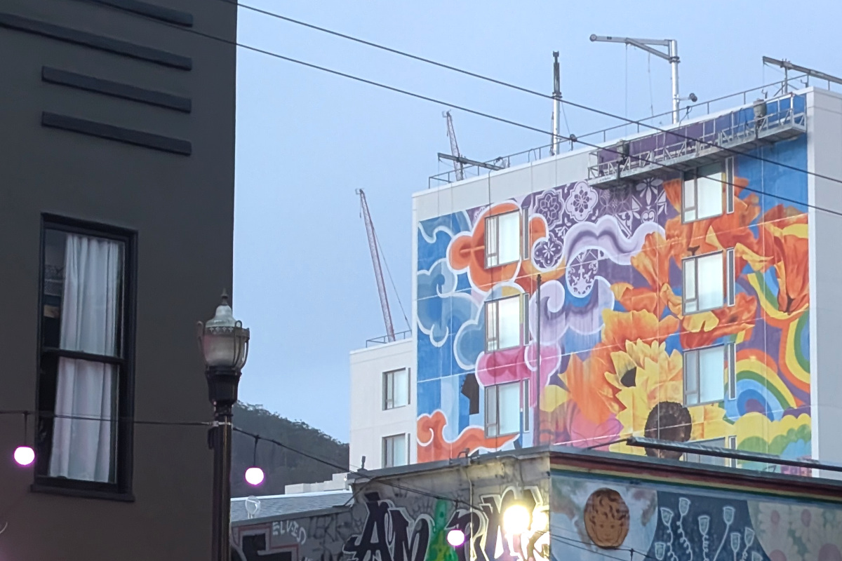 hemmed in by other buildings, we see a mural taking shape on the eastern exterior wall of the new building at Haight/Stanyan. The mural has clouds styled as in an old-timey Chinese painting, sunflowers, poppies, rainbows. Some purple geometrical designs with 8-way symmetry. It's pretty bright and colorful