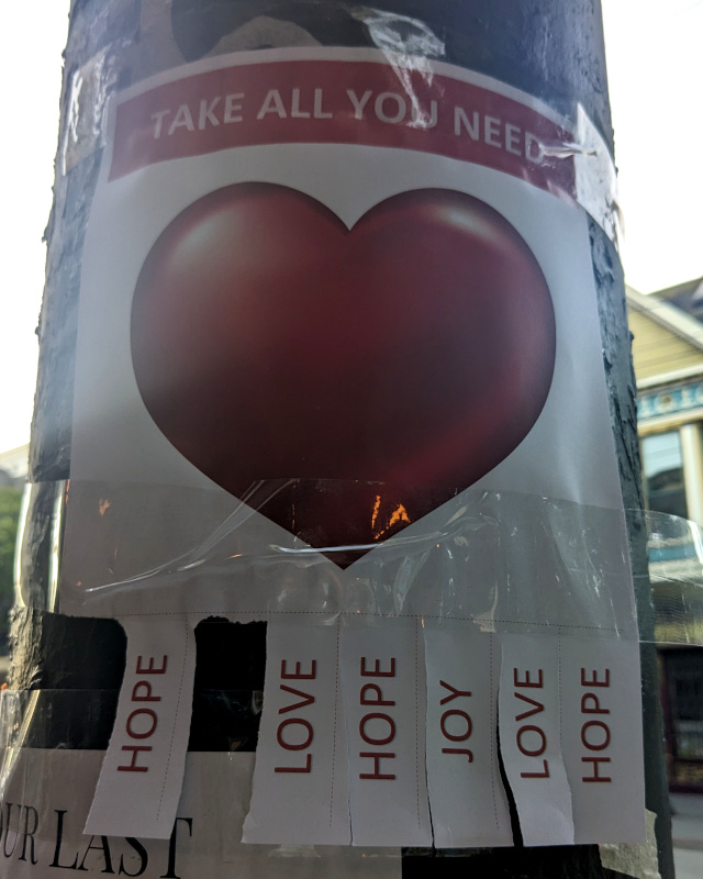 flyer posted on lightpole. flyer has text 'Take all you need ❤️'. Flyer has tear strips. You might expect contact info on the tear strips, but instead are words: Love, Hope, Joy