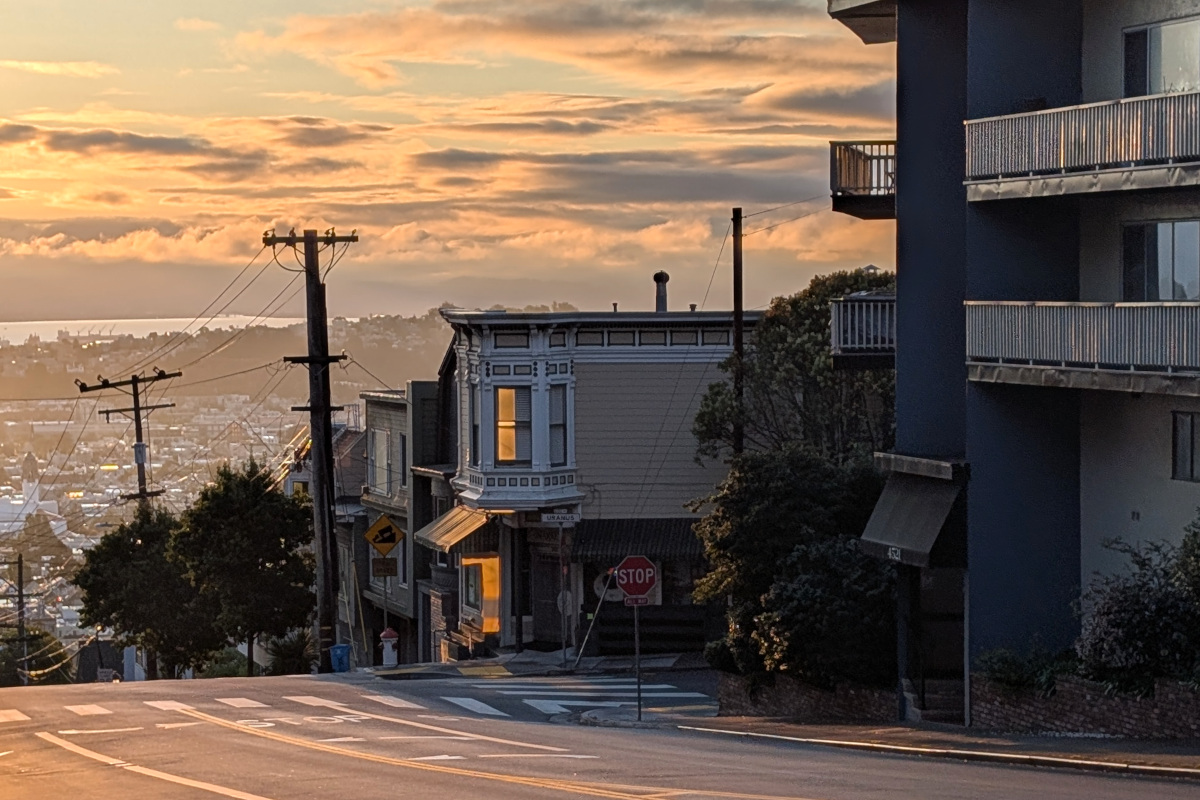 sunrise-y clouds behind the intersection of 17th St and Uranus, where a bodega nestles in shadow