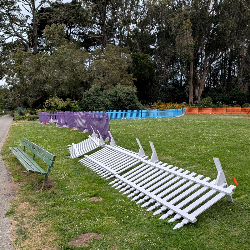 a big lawn with some temporary wooden picket fence set up; some of that fence has been blown over