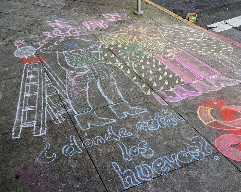 sidewalk chalk art. pretty surreal. an anthropomorphized egg has climbed a ladder and addresses a few neighbors. text below reads ¿dónde están los huevos?. text above is in Chinese which I can't read, but when I plugged 'where are the eggs?' into Google translate and tried a few dialects, I noticed the Traditional Chinese translation had a few characters in common. The neighbors... Well, there's a lady with a cloud head carrying a turnip. There's a caftan-wearing rainbow-headed figure carrying a chard? kale? leaf. There's a ✳-headed figure carrying a loaf of bread. There's a potato-bodied person covered with human eyes. The potato-eyes thing makes me wonder if I'm overlooking puns in the other figures. Off the the side, mostly out of frame: a snake (Happy New Year!)