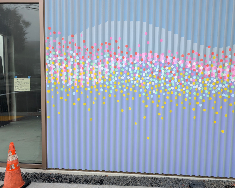 wall with mural consisting of different-colored circles on a background of a geometrical regular wave. Below, some still-under-construction pavement and a traffic cone. To the side, a window with a little piece of paper; if this image were higher resolution, you'd see that the paper tells you that Jenifer Wofford and others made the mural