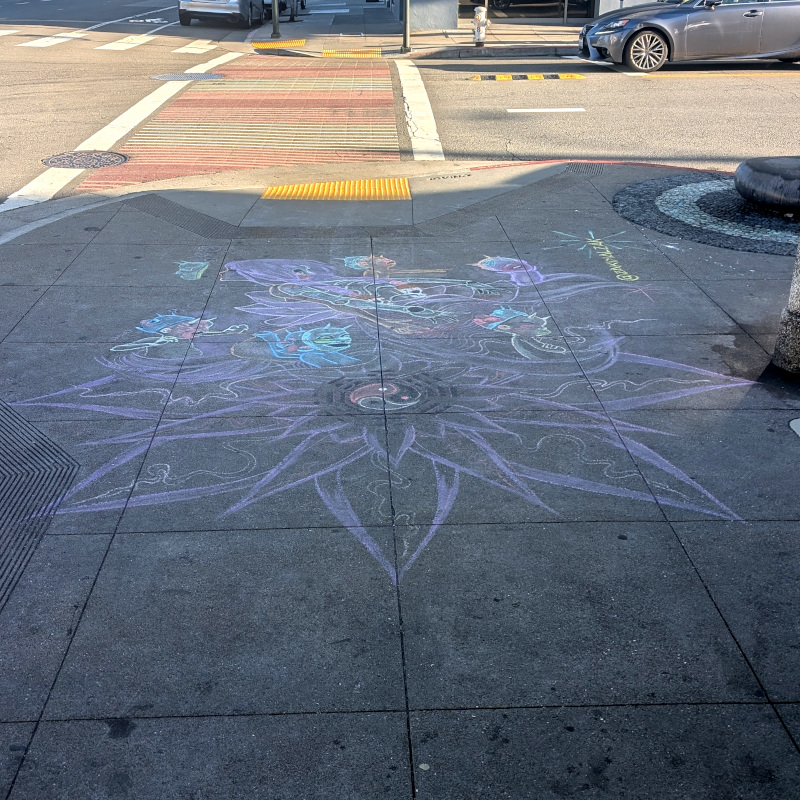 sidewalk chalk art: sidewalk at street corner. chalk art: a big purple flower with things coming out of it