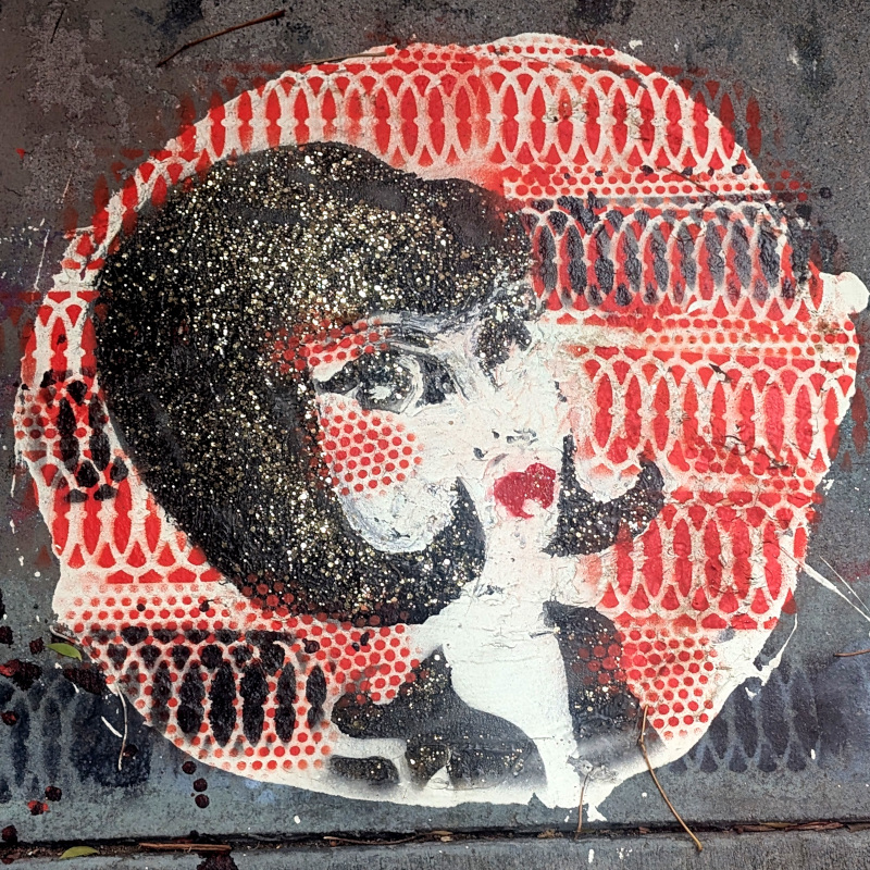 paint on sidewalk. there's lady's head with a patterned background. the hair's paint looks worn down, but IRL it's in good shape with a lot of glitter, sorry