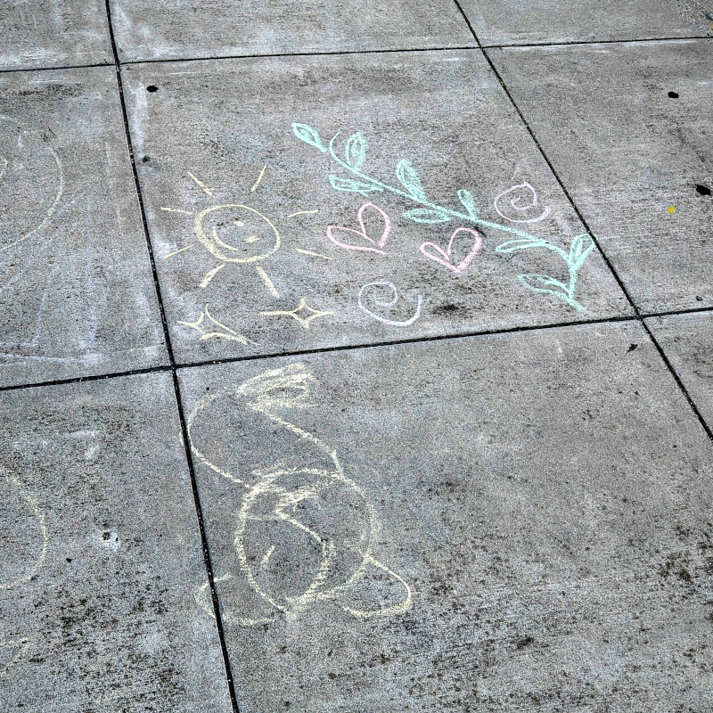 sidewalk chalk art: scribble open to interpretation; also a smiling sun face 🌞, a sprig of greenery, hearts ♡, sparkles ✨️, spirals