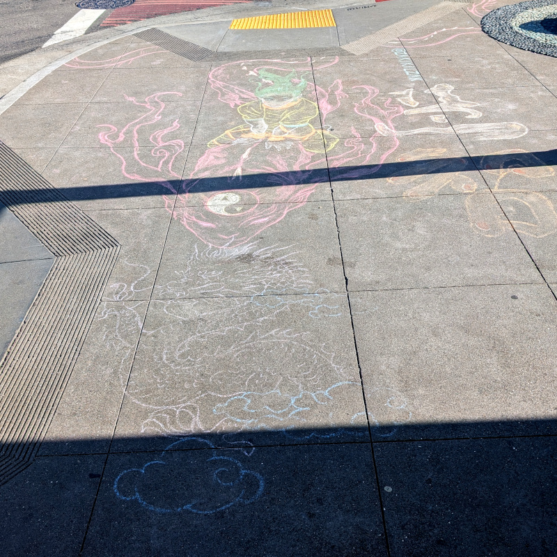 sidewalk chalk art: human-ish figure rides a flying dragon. they are headed towards another dragon, a faint outline. (Maybe this artwork isn't done yet? I wonder if the artist plans to color that second dragon in). On the side, there is some very fancy Chinese calligraphy that I, alas, do not understand and thus won't attempt to transcribe here