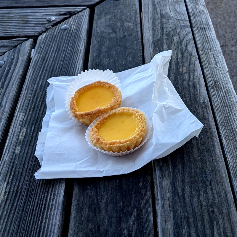 two little egg tarts on a paper bag on a bench. humble but yummy