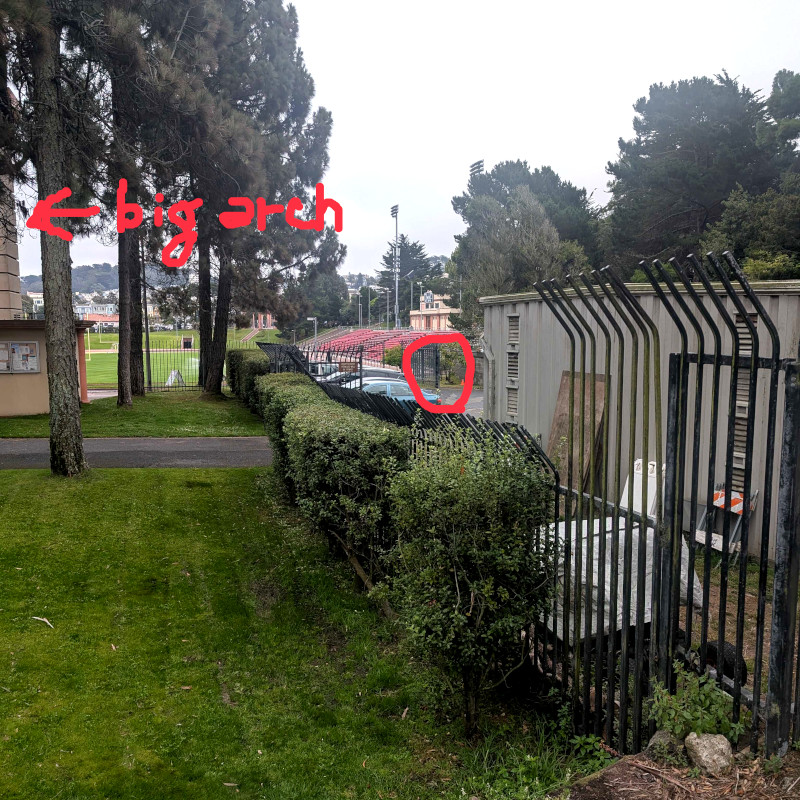 altered photo: path, lawn, fence, hedge, the edge of a big arch, and an ornament-thing. the alteration: someone has circled the ornament-thing and also written 'big arch' with an arrow pointing to the edge of the big arch