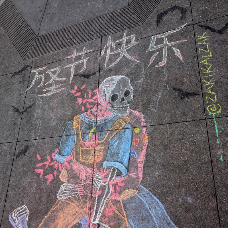 sidewalk chalk art: top of the artwork. you can see that one ghost has a skeleton arm but otherwise as made up of falling flower petals or something. the other ghost is more skeletal