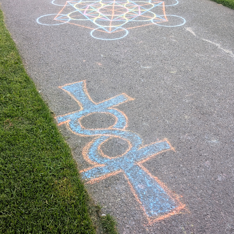 sidewalk chalk art: a couple of ankhs drawn with their loops touching to form a lemniscate, an infinity symbol. also part of another piece, a geometric construction of circles, hexagons, and triangles