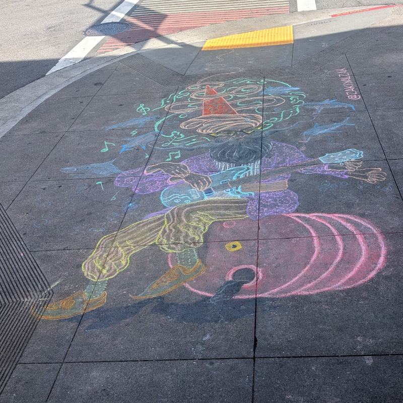 sidewalk chalk art: a guitarist sits on an oil drum. there's something mystical about him: he has more arms than you'd expect.