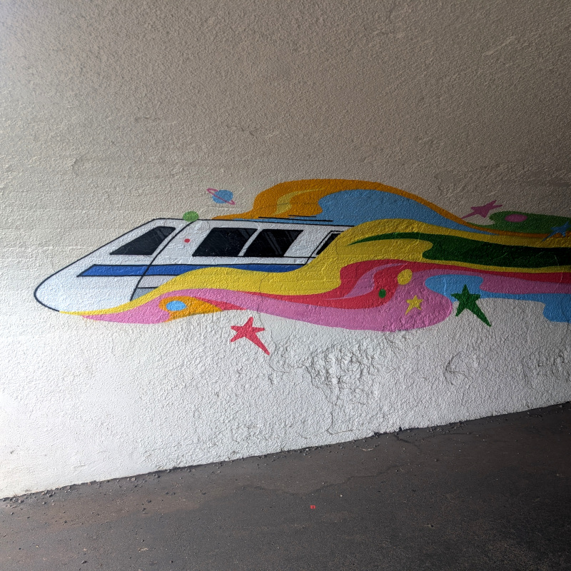 mural fragment: nose of a BART train whooshes along leaving a wispy trail of color behind