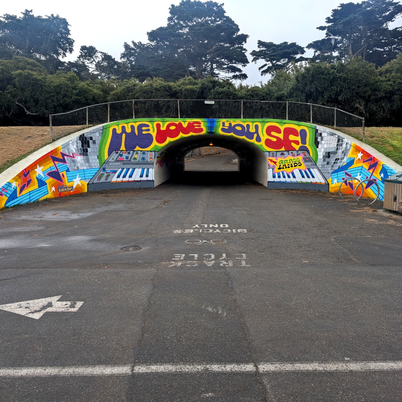 graffiti-looking mural around a tunnel entrance says 'we love you SF!' with images of a musical staff, a music synth, disco balls, notes