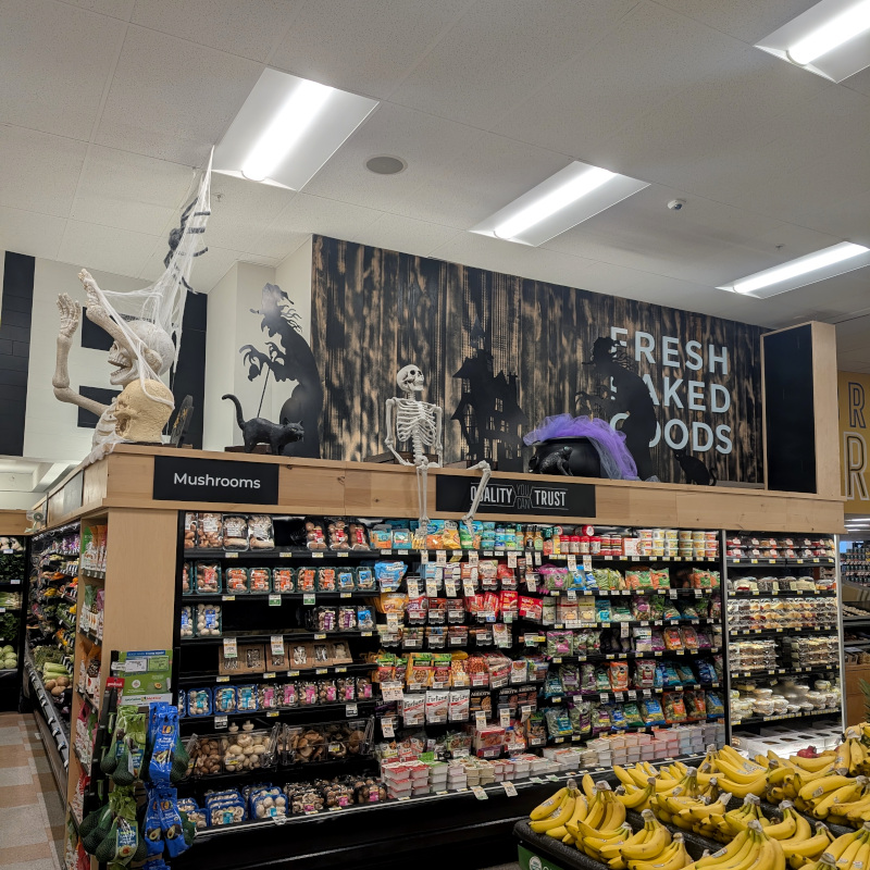 supermarket display case above which are some Hallowe'en decorations: skeletons, gravestone, witch silhouettes, etc