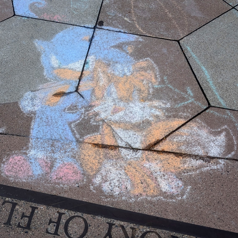 sidewalk chalk art: Pretty scuffed (alas) but still recognizable Sonic the Hedgehog. And if that's Sonic, then the orange blob next to him should be Tails the fox, right?