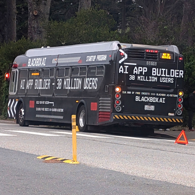 stalled bus pulled over by the side of the road. the bus' exterior is wrapped in ads for an 'AI App Builder'. See, the joke is that a lot of these AI companies meter their services as 'tokens' and it's a hassle when you run out. And buses used to use tokens. Hilarious, right? OK, maybe you had to be there