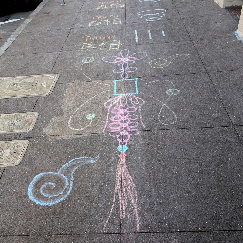 sidewalk chalk art: a few repititions of English text "truth" over some Chinese text "真理" which teh internets tells me means truth-as-in-principle. Below is depicted a sort of tassel-y wall-hanging decoration which gets kinda abstract in the middle