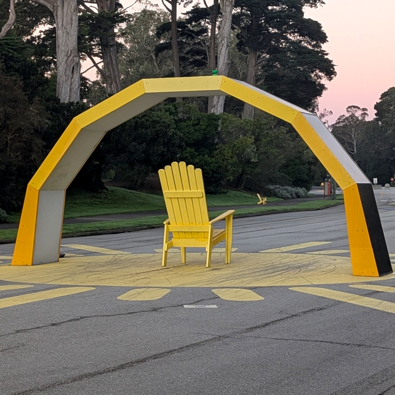 big yellow arch on paved road in a park. if you know where to look, there's a little green blob on top
