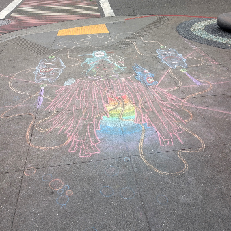 sidewalk chalk art. human figure. wearing a sort of shawl that might be made of strips of paper over a sort of rainbow glow. orbited by masks